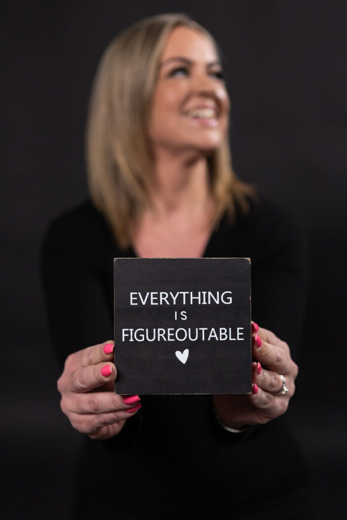 Woman smiling and holding a sign that reads "EVERYTHING IS FIGUREOUTABLE," emphasizing a positive mindset in digital marketing and growth strategies.